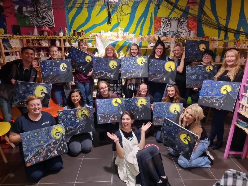 A big group holding up the canvases they painted at a team painting event