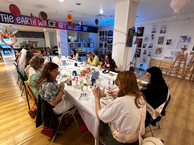 A group painting pottery together at long tables in the studio
