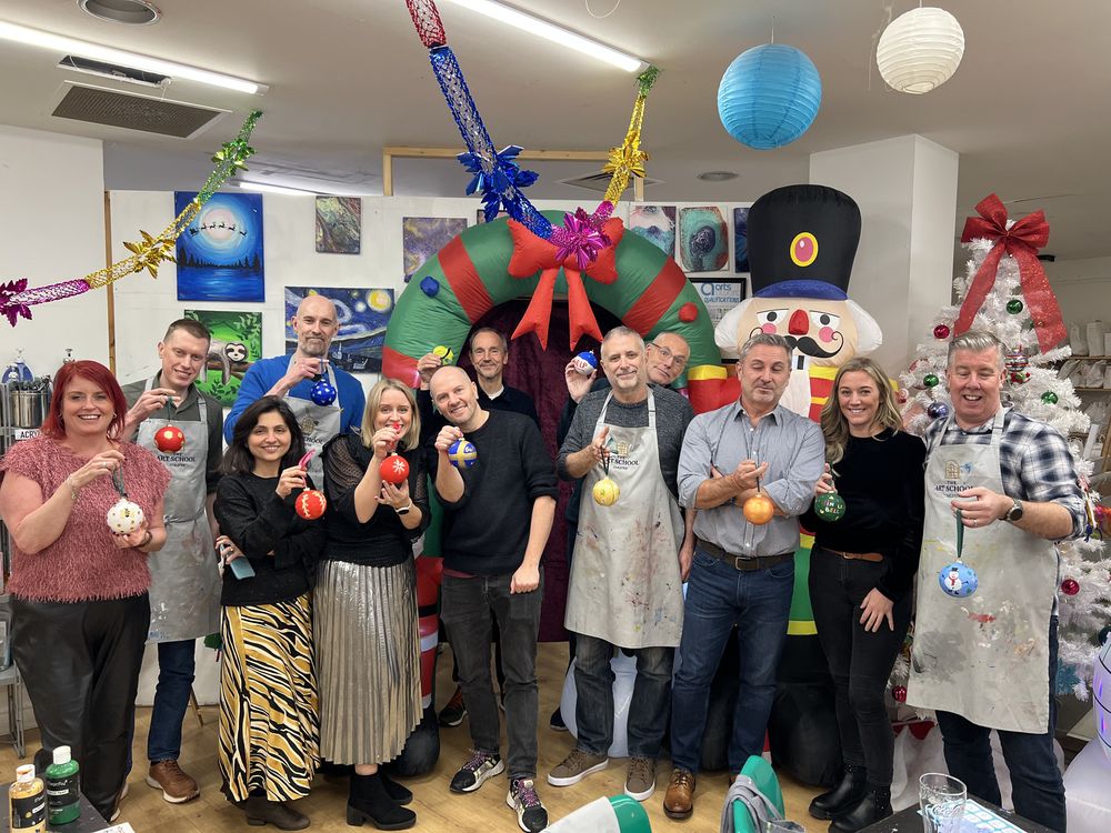 A work team in aprons holding the Christmas baubles they painted at their team event