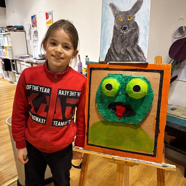 A smiling girl next to her monster painting at holiday art camp