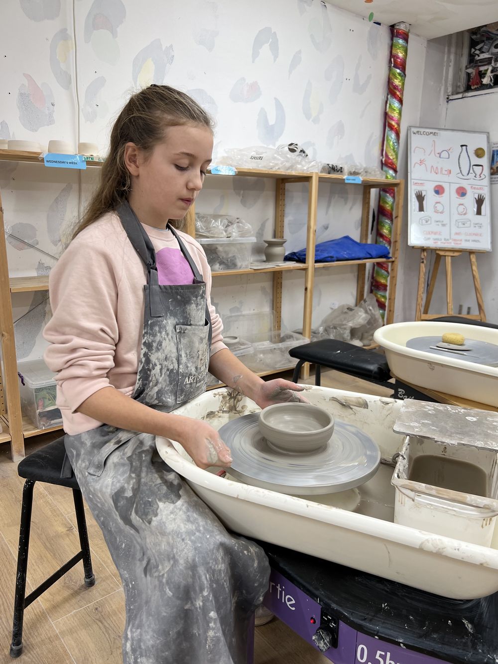 Young student in an apron centring clay on the pottery wheel