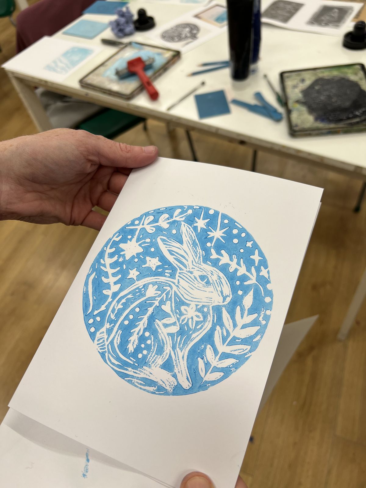 A hand-pulled blue lino print of a hare inside a wreath, held up in class